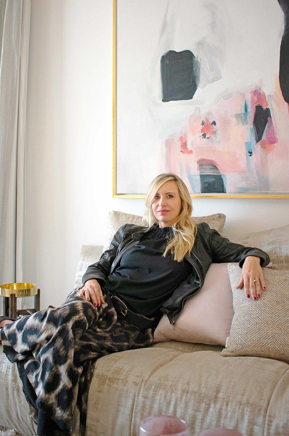 Andrea Bock relaxing on a sofa in a stylish Sotogrande living room, featuring modern abstract art and elegant decor.