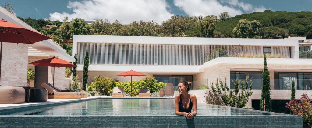 Woman enjoying a swim in an infinity pool at La Reserva Club with modern architecture and lush greenery in the background.