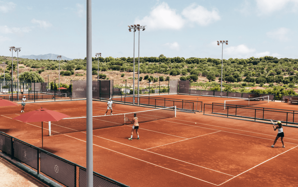 People playing tennis on clay courts at La Reserva Club with a scenic backdrop of greenery and hills.