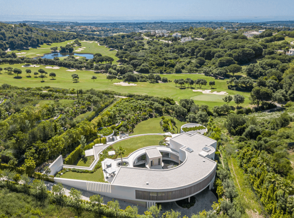 Aerial view of a modern luxury villa in Sotogrande surrounded by lush greenery and golf courses near the Mediterranean coast.